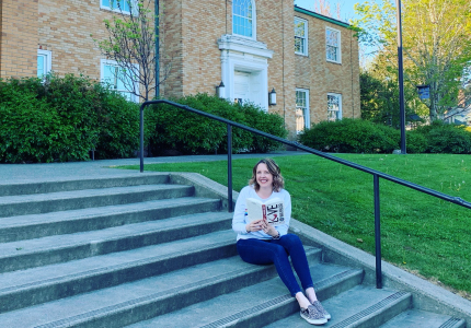 woman sitting on steps in front of the library building holding a book