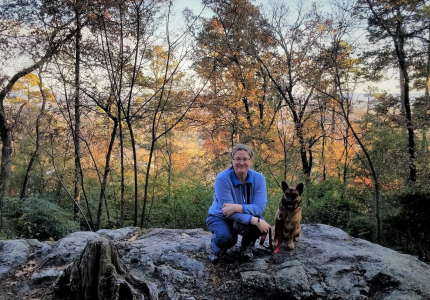 woman kneeling next to a leashed dog on top of a rock