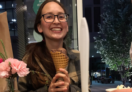 Woman holding an ice cream cone, behind a scoop of ice cream in a cup with a spoon sticking out of it