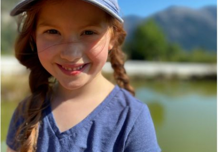 Little girl with a purple hat and shirt smiling in the sun