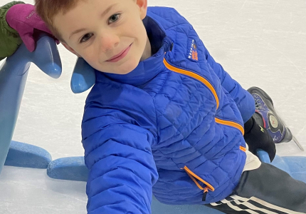 A boy in a blue jacket sitting on a sled in an ice rink
