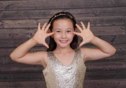 A smiling girl in a sparkly dress with her hands framing her face