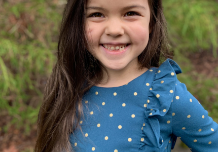 A smiling little girl in a blue polka dot shirt