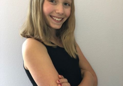A blond smiling girl angled to the side with arms crossed 
