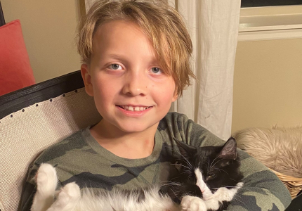 A boy smiling and holding a black and white cat