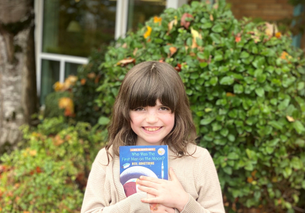 A girl holding a book outside.