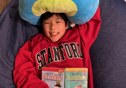 Bryson laying on a bean bag chair with a book and a large squish toy.