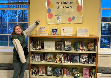 Cora proudly gesturing to her Kid Librarian display.