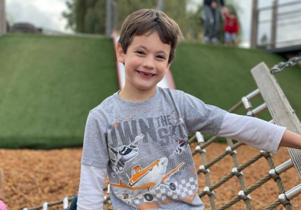 Bowen on a playground smiling next to a play structure.