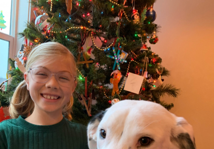 Eleanor sitting in front of a Christmas tree next to a white dog