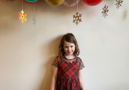 Zia standing under red, green, and gold balloons.