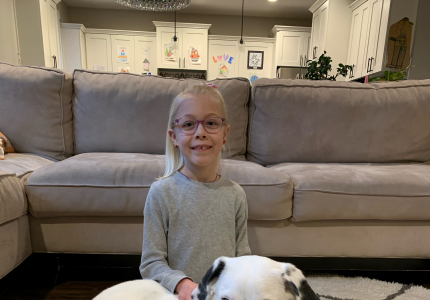 Adeline sitting in front of a gray couch next to a white dog.