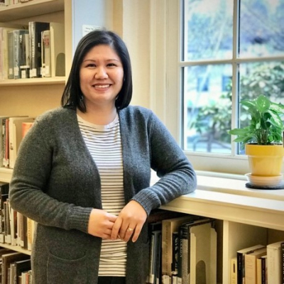 woman standing in front of bookcase with a window in the background