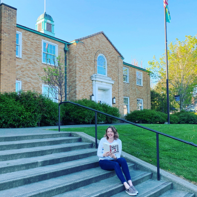 woman sitting on steps in front of the library building holding a book