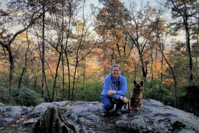 woman kneeling next to a leashed dog on top of a rock