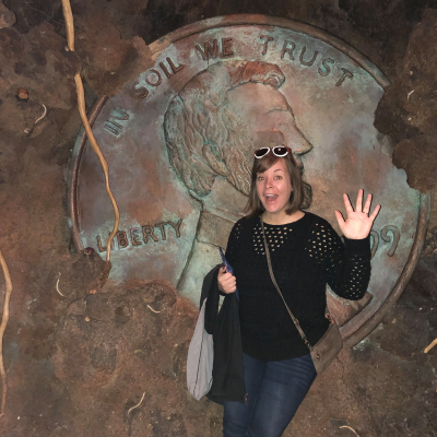 woman standing in front of a largescale penny embedded in a wall