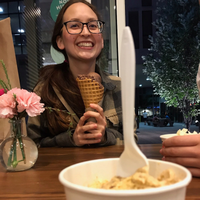 Woman holding an ice cream cone, behind a scoop of ice cream in a cup with a spoon sticking out of it