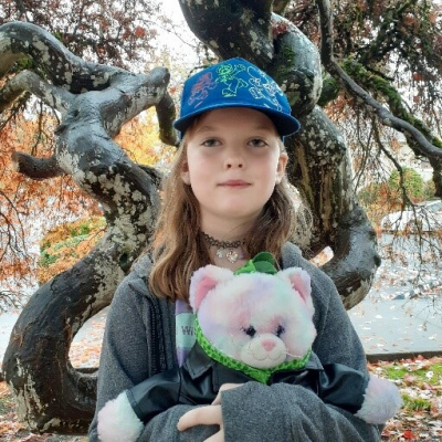 A blond child holding a plush animal standing in front of a tree