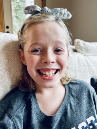 Girl with a hairbow smiling and sitting on a couch