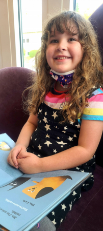 Little girl sitting on a big chair, smiling with an open book in her lap