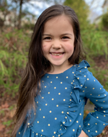 A smiling little girl in a blue polka dot shirt