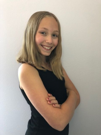 A blond smiling girl angled to the side with arms crossed 