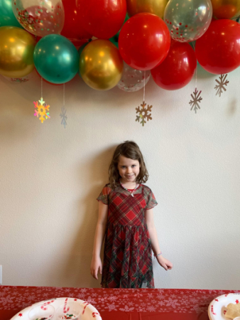 Zia standing under red, green, and gold balloons.